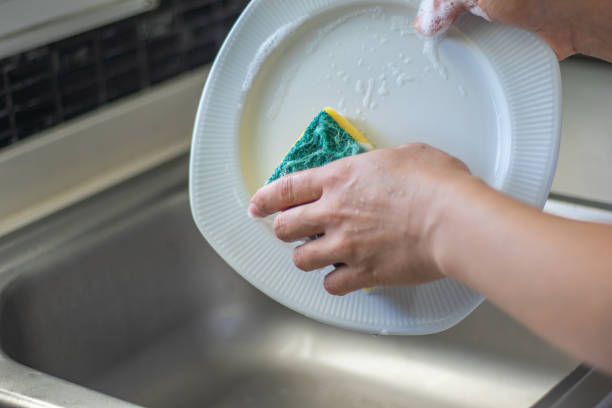 istock Young woman washing dishes with a sponge 1268260436