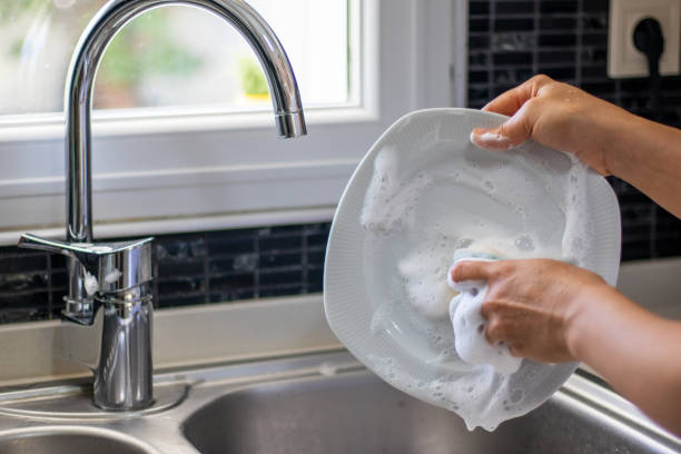 junge frau waschen geschirr mit einem schwamm - abwaschen stock-fotos und bilder