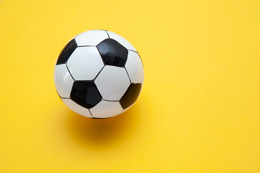 Miniature black and white football on a plain yellow surface with copy space to the right