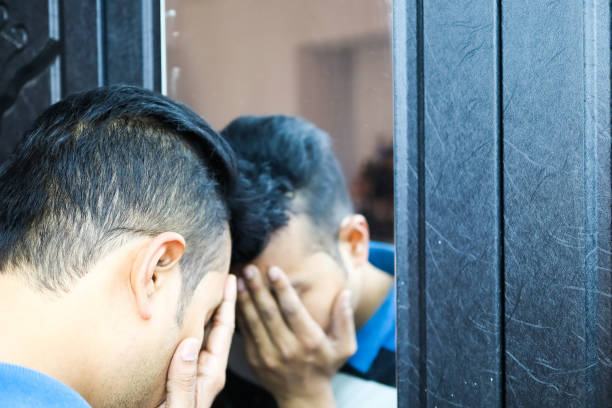 a man with hands on his face in front of a mirror in depressed mood with selective focus on mirror image.