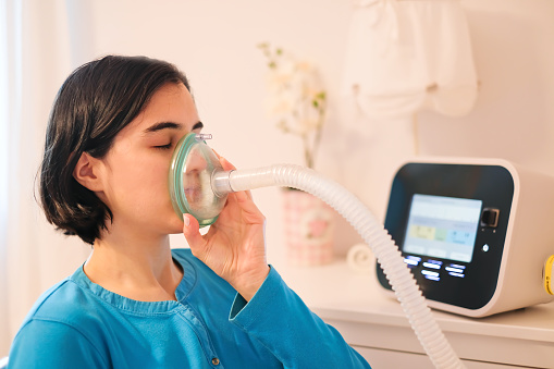 Una mujer caucásica que usa una mascarilla de ventilación de asistencia para la tos para respirar profundamente, afección respiratoria photo