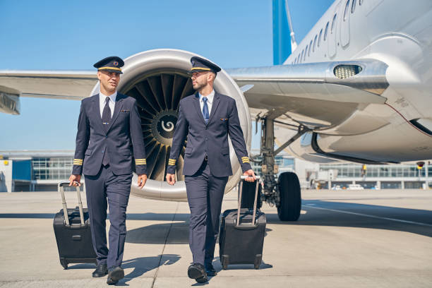 Two airline male pilots and their baggage Full-length portrait of young Caucasian airmen in uniforms pulling their trolley bags across the airdrome pilot stock pictures, royalty-free photos & images