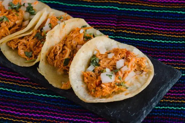 Photo of Mexican tacos filled with tinga de pollo on a traditional textile background