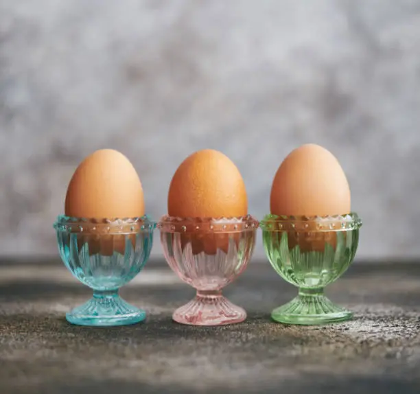 Still life image of brown eggs in pastel colored glass eggcups