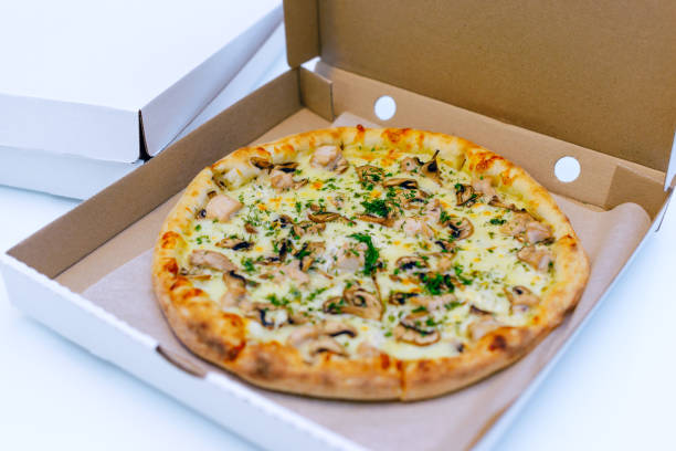 istock Pizza in a cardboard box on a light background. Top view. Pizza delivery. Pizza menu. Pizza on the kitchen table. 1268288104