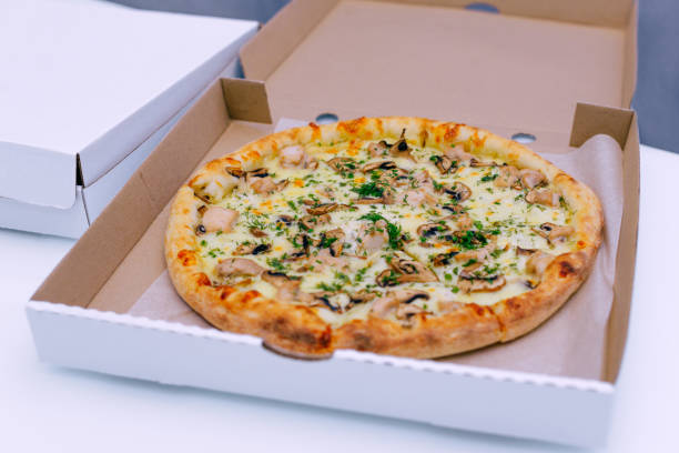 istock Pizza in a cardboard box on a light background. Top view. Pizza delivery. Pizza menu. Pizza on the kitchen table. 1268288108