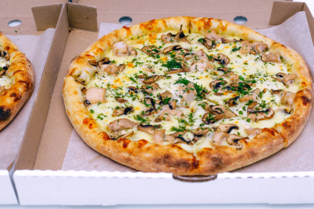 istock Two pizzas in a cardboard box on a light background. Top view. Pizza delivery. Pizza menu. Pizza on the kitchen table. 1268288109