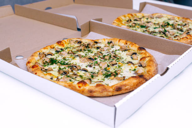 istock Two pizzas in a cardboard box on a light background. Top view. Pizza delivery. Pizza menu. Pizza on the kitchen table. 1268288115
