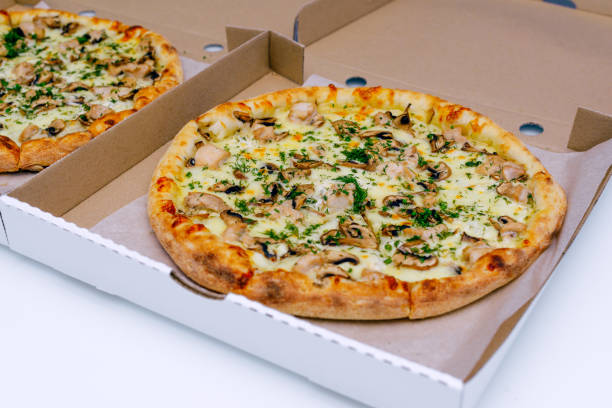istock Two pizzas in a cardboard box on a light background. Top view. Pizza delivery. Pizza menu. Pizza on the kitchen table. 1268288121