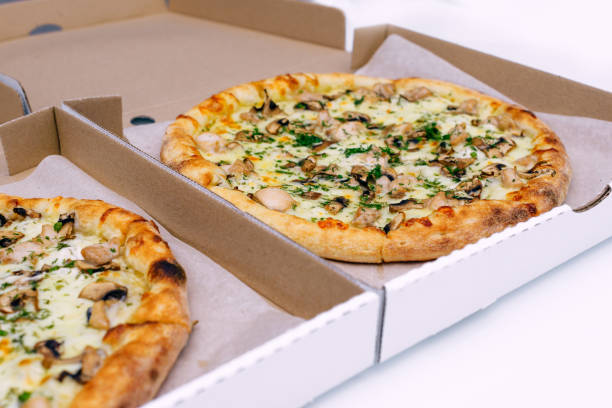 istock Two pizzas in a cardboard box on a light background. Top view. Pizza delivery. Pizza menu. Pizza on the kitchen table. 1268288125