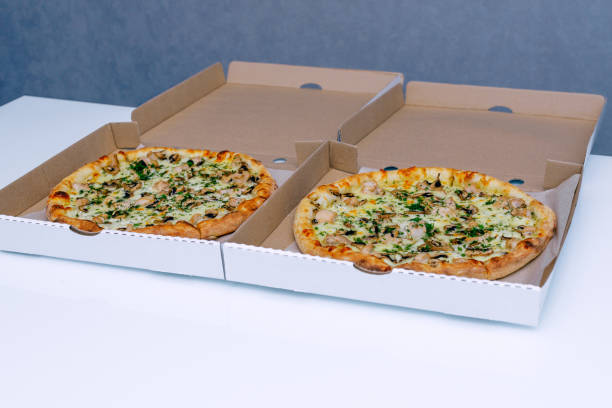 istock Two pizzas in a cardboard box on a light background. Top view. Pizza delivery. Pizza menu. Pizza on the kitchen table. 1268288130