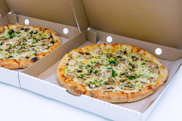istock Two pizzas in a cardboard box on a light background. Top view. Pizza delivery. Pizza menu. Pizza on the kitchen table. 1268288137