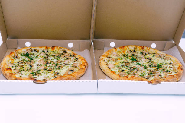istock Two pizzas in a cardboard box on a light background. Top view. Pizza delivery. Pizza menu. Pizza on the kitchen table. 1268288147