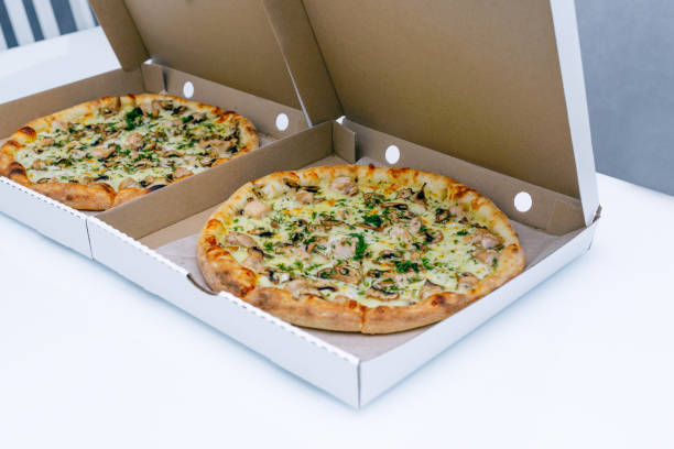 istock Two pizzas in a cardboard box on a light background. Top view. Pizza delivery. Pizza menu. Pizza on the kitchen table. 1268288149