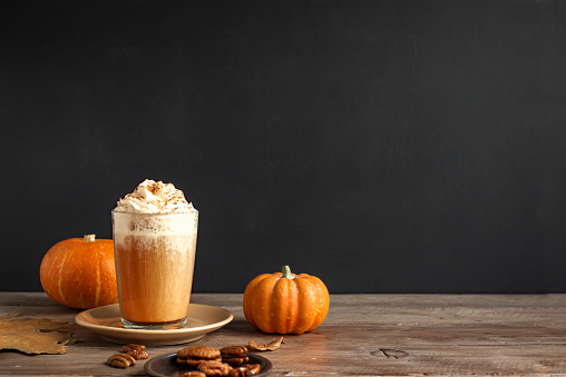 Pumpkin Spice Latte. Seasonal coffee drink and organic pumpkins near black wall, copy space.