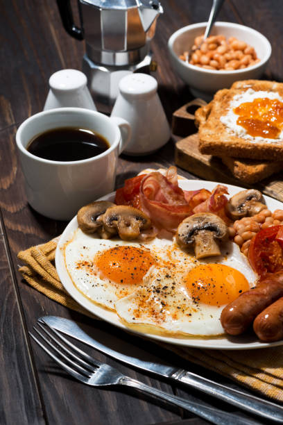 istock Fried eggs with bacon, sausages and vegetables for breakfast, vertical 1268288996