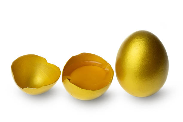 istock Golden eggs and half broken egg with yolk isolated at the white background 1268290266