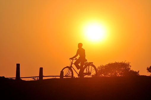 A young village boy enjoys his cycle ride in the golden glow of dusk in a remote village in North Bengal, India.