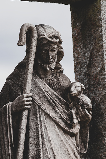 Dark contrast image of Jesus figure holding baby lamb and Shepard’s crook cane