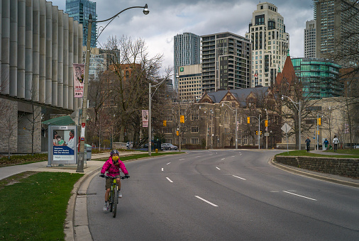 Toronto, Canada - April 11, 2020:  Biker with a protective face mask  is riding a bike on empty from cars Queens Park Crescent due to the COVID 19 pandemic