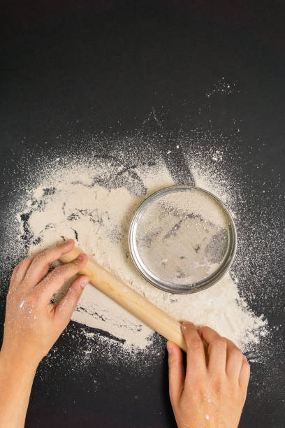 istock Males hands sprinkle with flour a wooden table for making dough, topview. on black background. vertical photo 1268294739