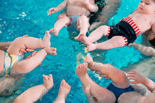 un groupe de mères avec leurs jeunes enfants dans un cours de natation pour enfants avec un entraîneur. - water touching sensory perception using senses photos et images de collection