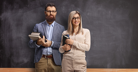 Male and female teacher standing in front of a school blackboard and holding books