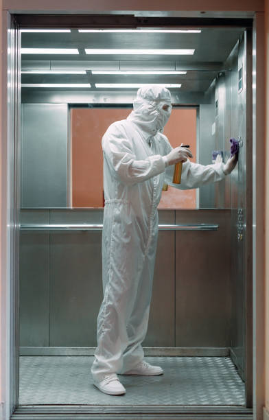 istock Coronavirus infection. Paramedic in protective mask and costume disinfecting an elevator with sprayer, 1268300922