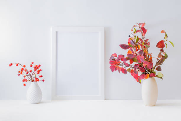 istock Home interior with decor elements. Mockup with a white frame, colorful autumn leaves in a vase on a light background 1268302896