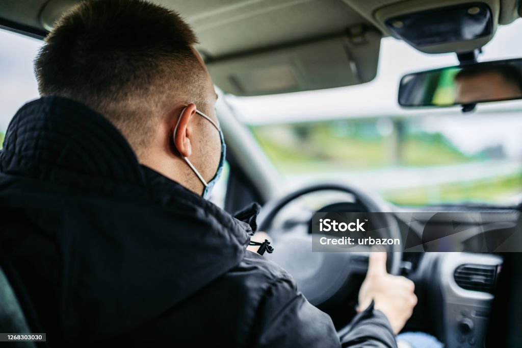 Man driving car with mask Caucasian serene man driving car through city and wearing protective face mask. Taxi Driver Stock Photo