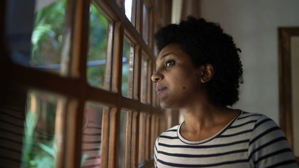 istock Mature women looking through window contemplating and thinking at home 1268303872