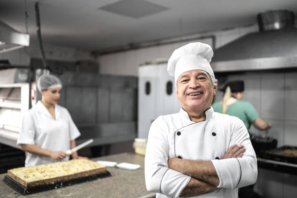 Portrait of a confident senior baker standing in a commercial kitchen with arms crossed Portrait of a confident senior baker standing in a commercial kitchen with arms crossed confectioner photos stock pictures, royalty-free photos & images
