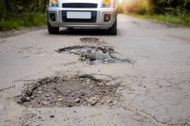 Road in terrible condition. Photo of a road with many potholes, chuckholes and driver driving the car very slow in order not to damage his vehicle stock photo