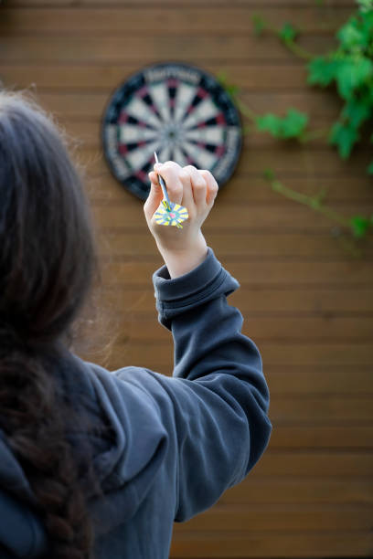 unerkennbare mädchen mit dem rücken zu uns mit dartpfeil in der hand zielt auf ein darts zielbrett. zielkonzept - aiming challenge business throwing stock-fotos und bilder