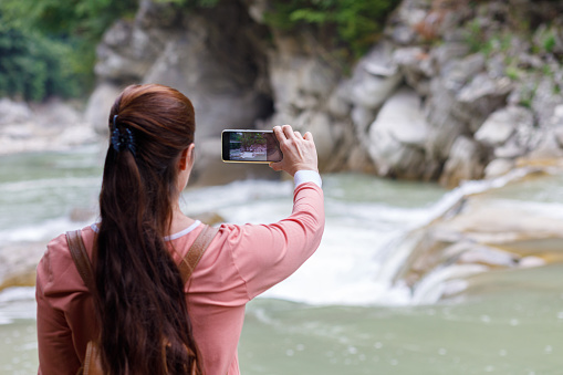 Woman tourist photographs a mountain river on the phone.