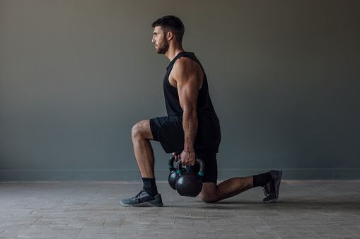 Muscular athlete doing cross training exercises with kettlebell weights, strength training concept.