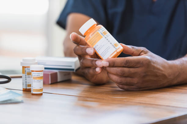 thuiszorgverpleegkundige bekijkt medicatie met patiënt - pillenpotje stockfoto's en -beelden