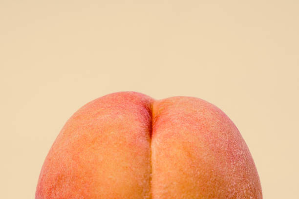 Fresh Peach on Peach Colored Background A detailed image of a freshly picked ripe peach.  Photographed on a peach colored background. buttock stock pictures, royalty-free photos & images