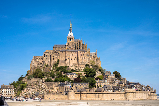 Beauvoir, France.  May 12, 2019.  Full view of the castle at Mont St. Michel with tourists milling around on the beach.