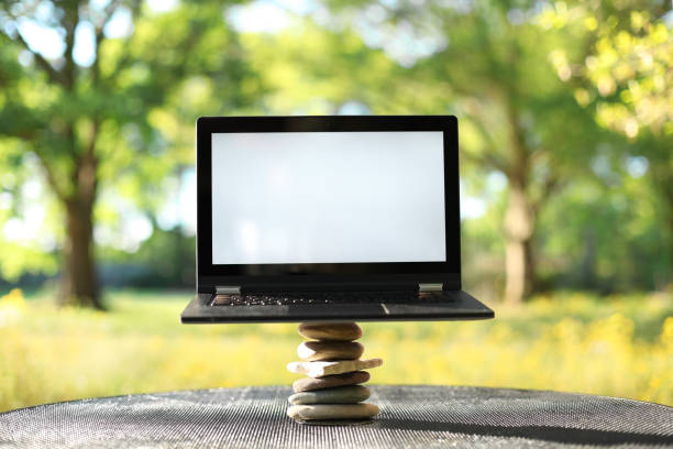 istock Laptop with blank screen outdoors balancing on stones surrounded by trees. Nature vs work life balance concept. 1268369714