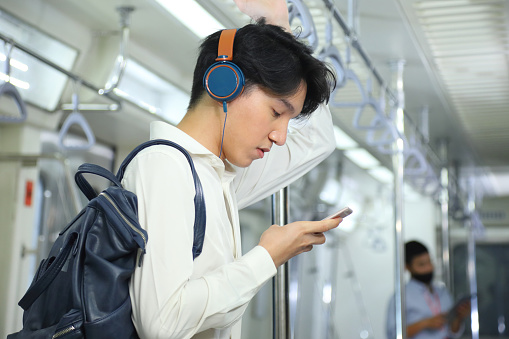 A lifestyle of young Asian man using cellphone with headset while taking the subway train to work at the rush hour morning with copy space