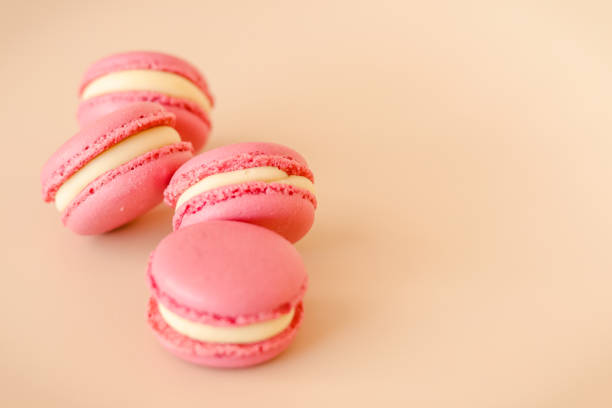 istock Four pink macaroon cookies with white chocolate cream on beige background 1268390929