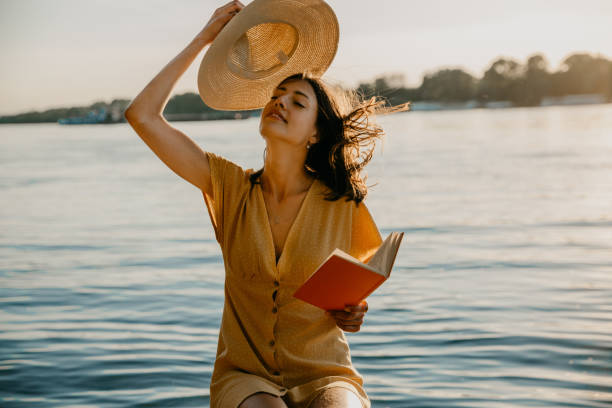 attraente bruna caucasica felice in un abito giallo vicino al fiume - beach women joy sand foto e immagini stock