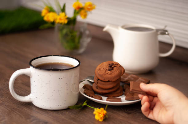 Woman hands with white kettle tea cup and choccolate cookie. Selective focus. Kitchen teatime. Time for rest and home bun-fight