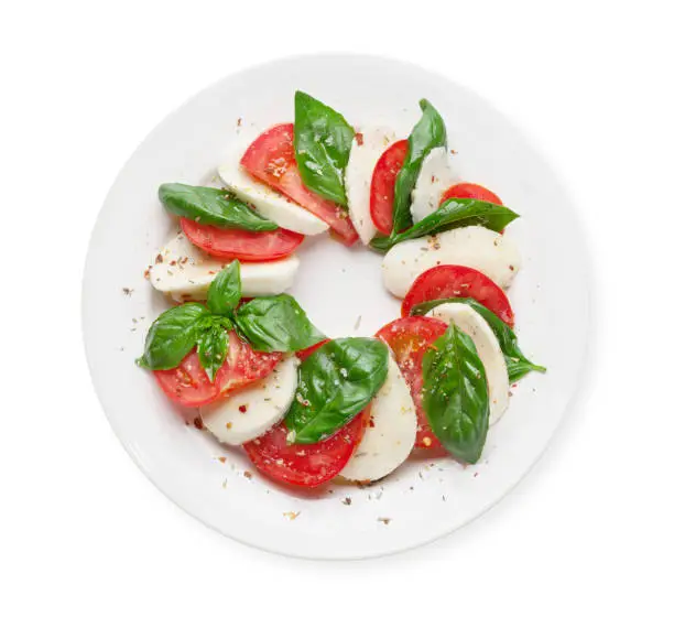 Caprese salad. Mozzarella cheese, tomatoes and basil herb leaves. Top view flat lay isolated on white