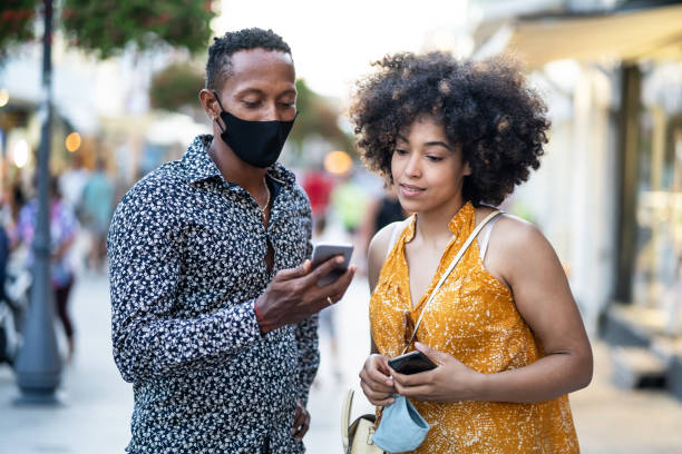 istock Afro Couple wearing protective face mask walking on the streets and using smart phone, during COVID-19 1268398297