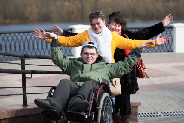 disabile su una sedia a rotelle con famiglia nel parco. un uomo con la sua famiglia su una sedia a rotelle - senior adult wheelchair community family foto e immagini stock