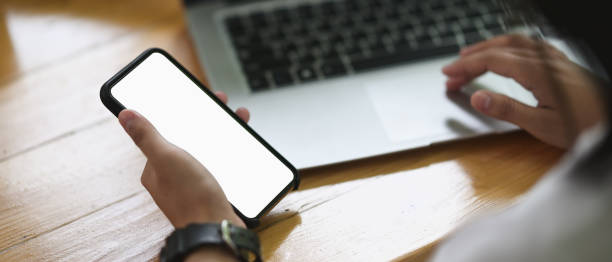 istock Cropped image of the hand is using a white blank screen mobile at the wooden table. 1268404819