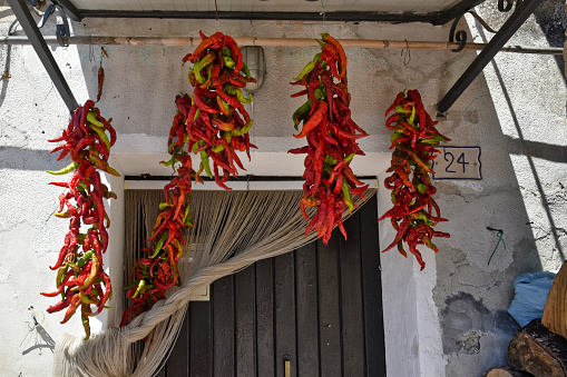 Altomonte, Italy, 08/13/2020. Red chillies hanging to dry in the sun on the doorstep in an old town in the Calabria region.