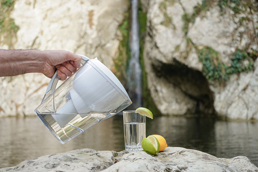 Water Pitcher. A man uses a jug with a filter to purify water against the background of a mountain river and waterfall